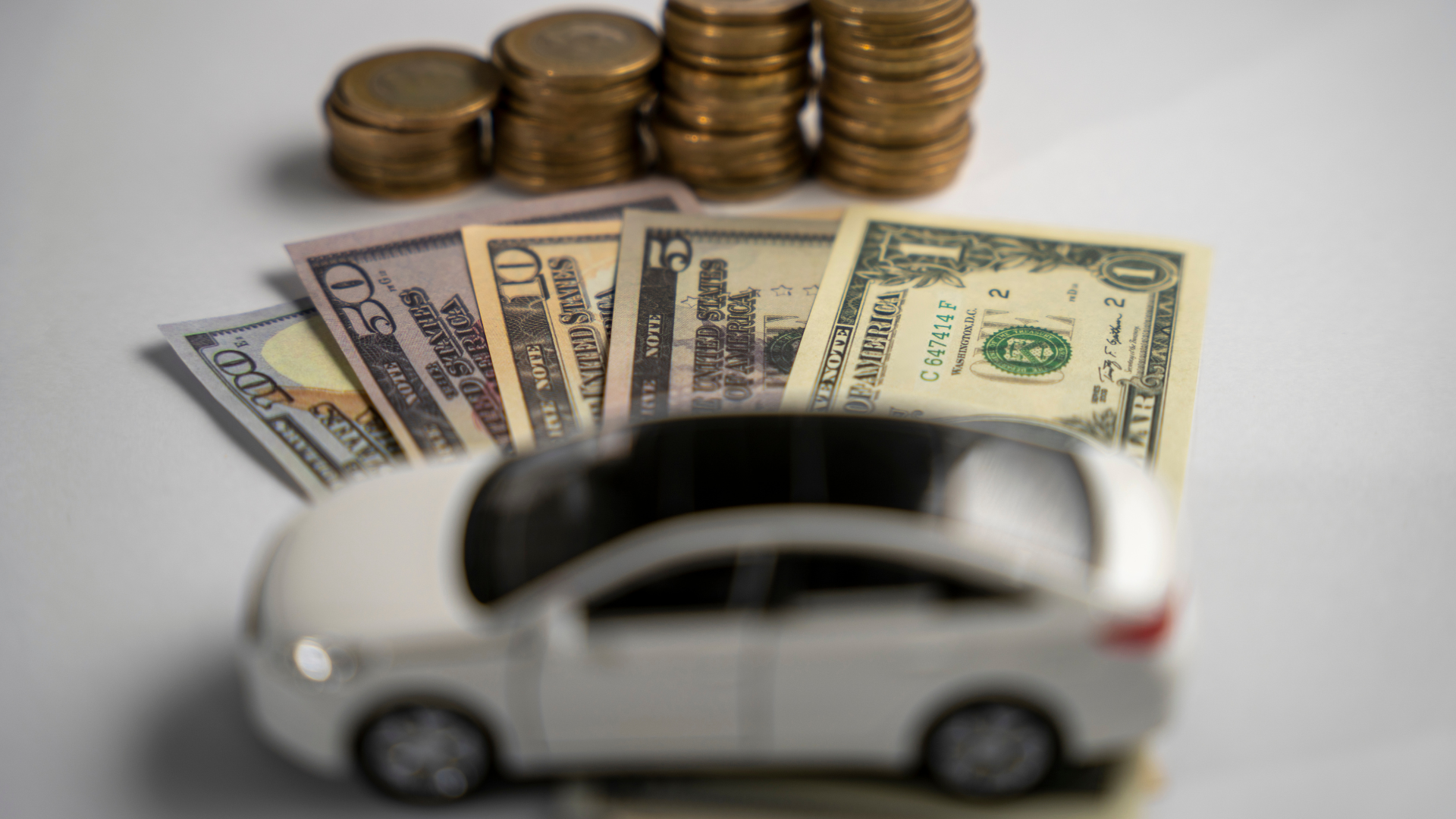 A toy car is sitting on top of a pile of money and coins.