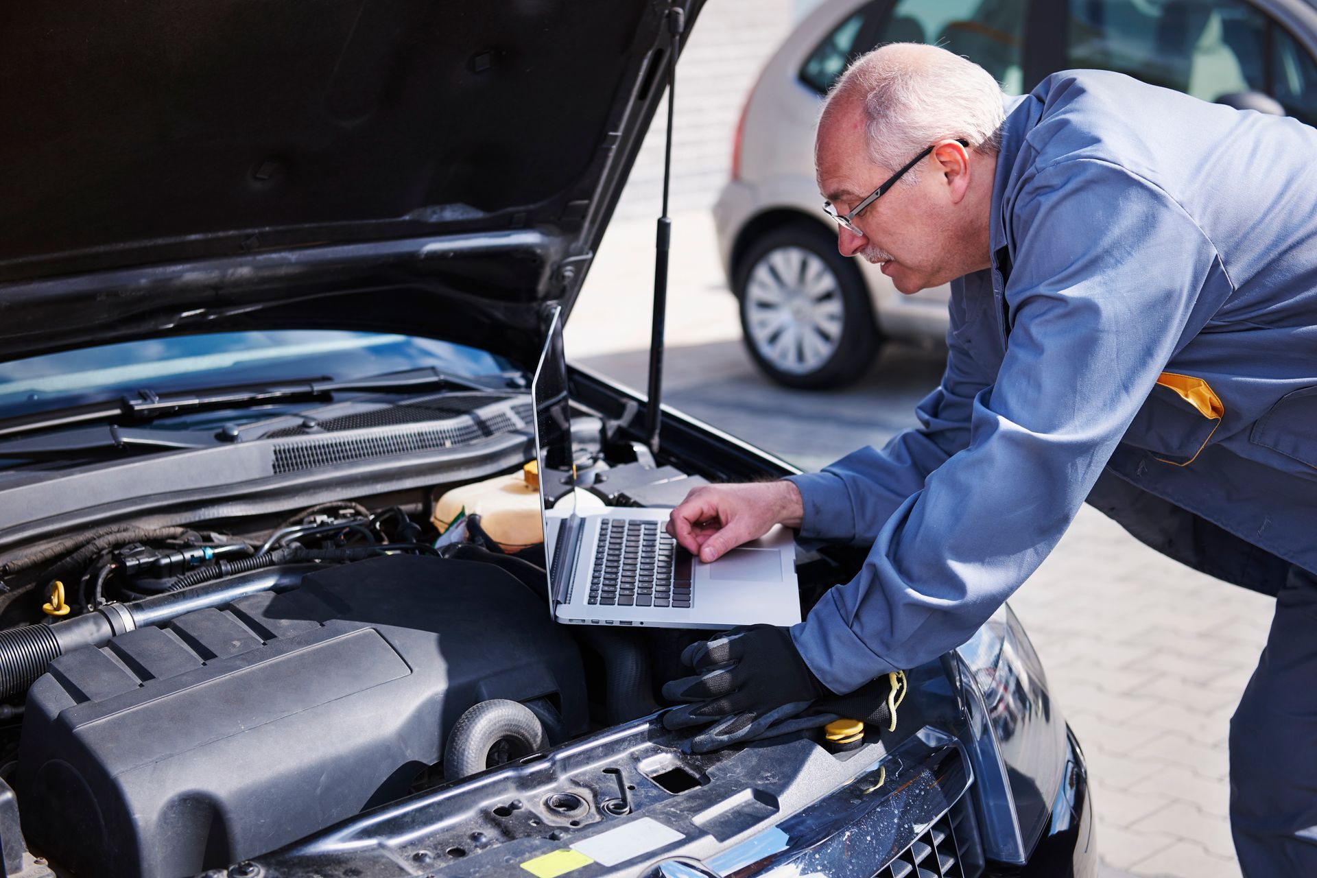 Mechanic with glasses using laptop to diagnose a car engine.