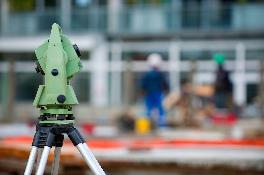 Surveying equipment on a tripod at a construction site, with blurred workers in the background.