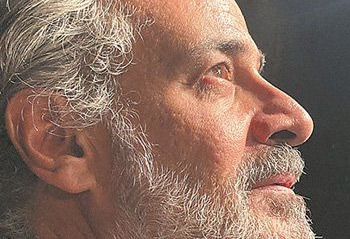 Γυναίκα με σκούρα μαλλιά, τα χέρια στο πρόσωπό της, κοιτάζει στο πλάι με ένα απαλό χαμόγελο.