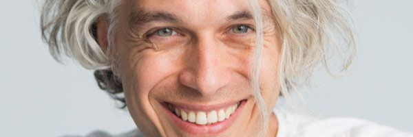 Γυναίκα με σκούρα μαλλιά, τα χέρια στο πρόσωπό της, κοιτάζει στο πλάι με ένα απαλό χαμόγελο.