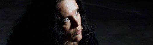 Γυναίκα με σκούρα μαλλιά, τα χέρια στο πρόσωπό της, κοιτάζει στο πλάι με ένα απαλό χαμόγελο.