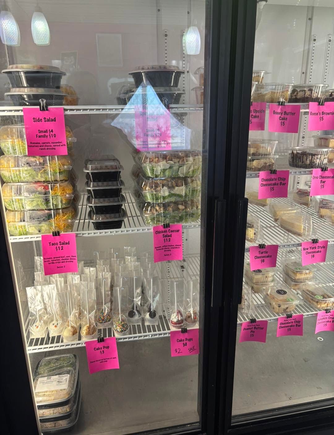 Glass display case with jars and packaged sweets, labeled with bright pink tags in a store.