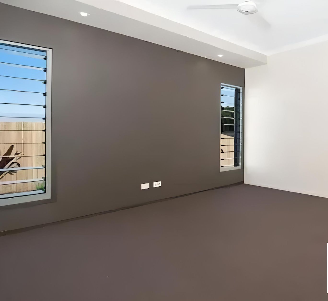 An Empty Room With Two Windows and a Ceiling Fan — O'Brien Painting Contractors in Alexandra Headland, QLD