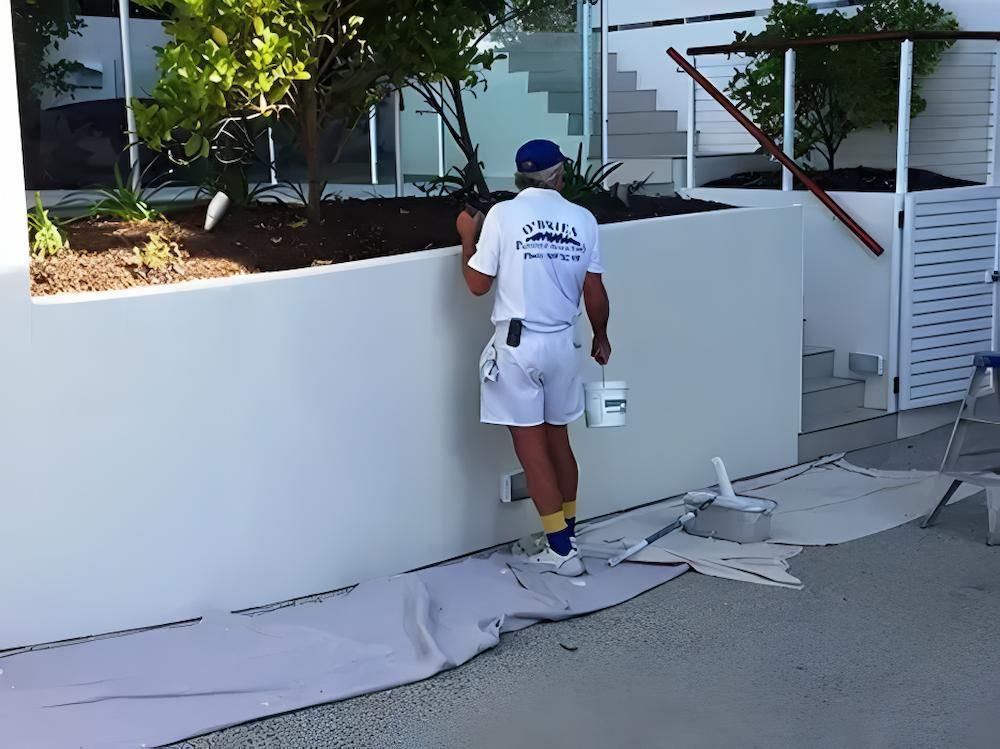 A Man is Painting a Wall With a Florida Painting Company Shirt on — O'Brien Painting Contractors in Alexandra Headland, QLD 