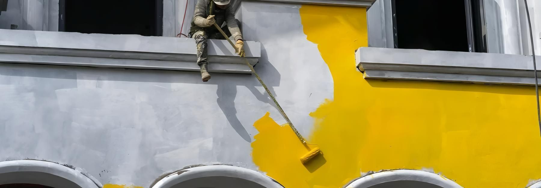 A Man is Painting a Building Yellow — O'Brien Painting Contractors in Alexandra Headland, QLD