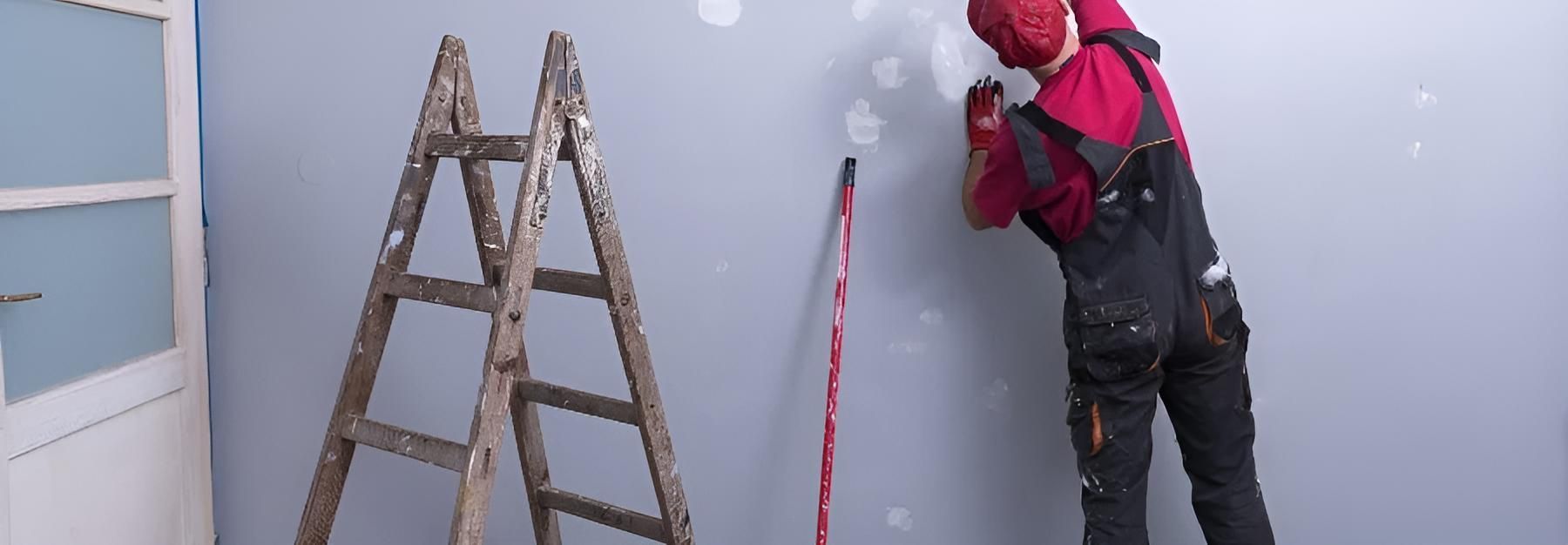 A Man is Painting a Wall Next to a Wooden Ladder — O'Brien Painting Contractors in Alexandra Headland, QLD
