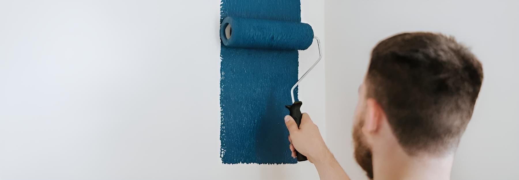 A Man is Painting a Wall With a Blue Paint Roller — O'Brien Painting Contractors in Alexandra Headland, QLD