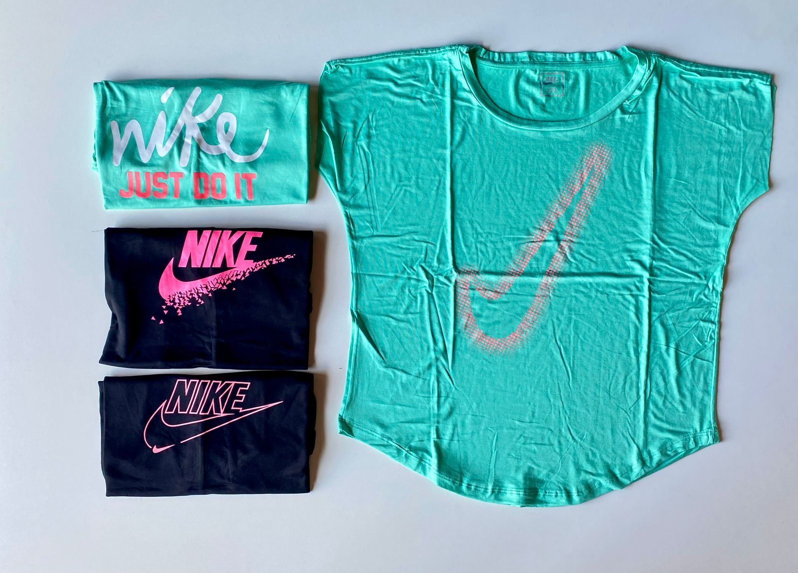 Una camisa verde claro con un gran logotipo de Nike junto a tres camisas dobladas en negro y verde con la marca Nike.