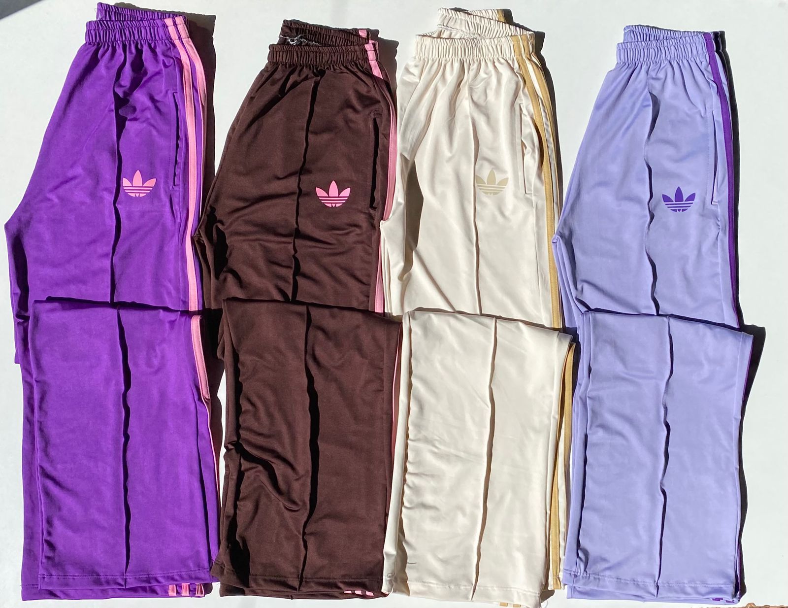 Cuatro pares de pantalones deportivos Adidas de color morado, marrón, crema y lavanda.