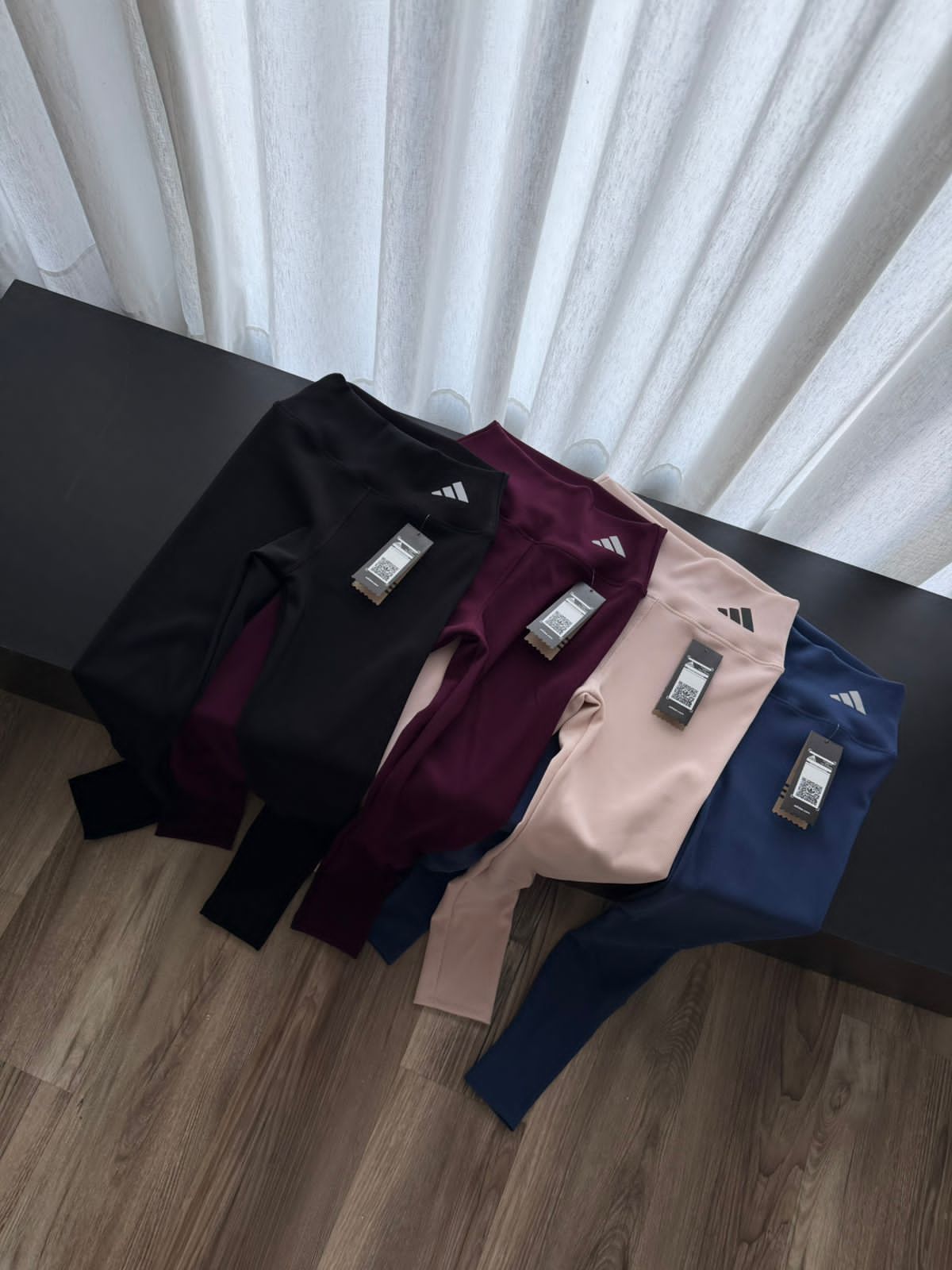 Cuatro pares de leggings Adidas doblados, de color negro, burdeos, beige y azul marino.