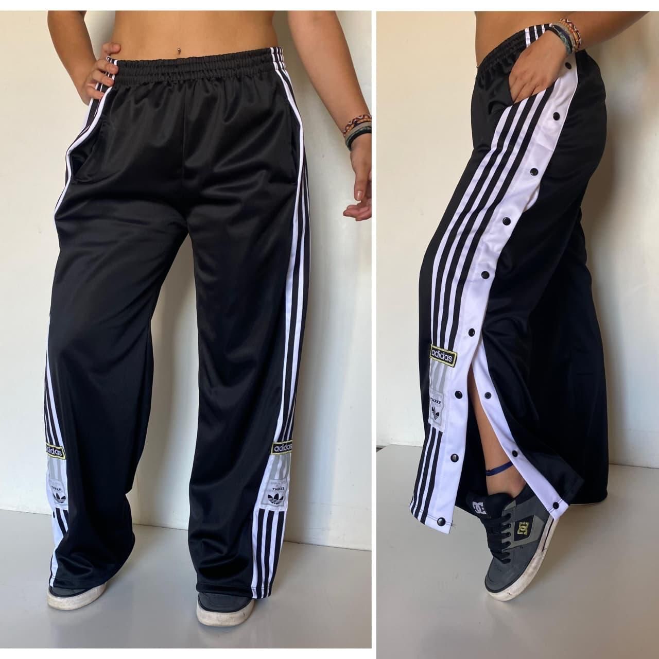 Una persona lleva un pantalón deportivo negro de Adidas con tiras laterales blancas.