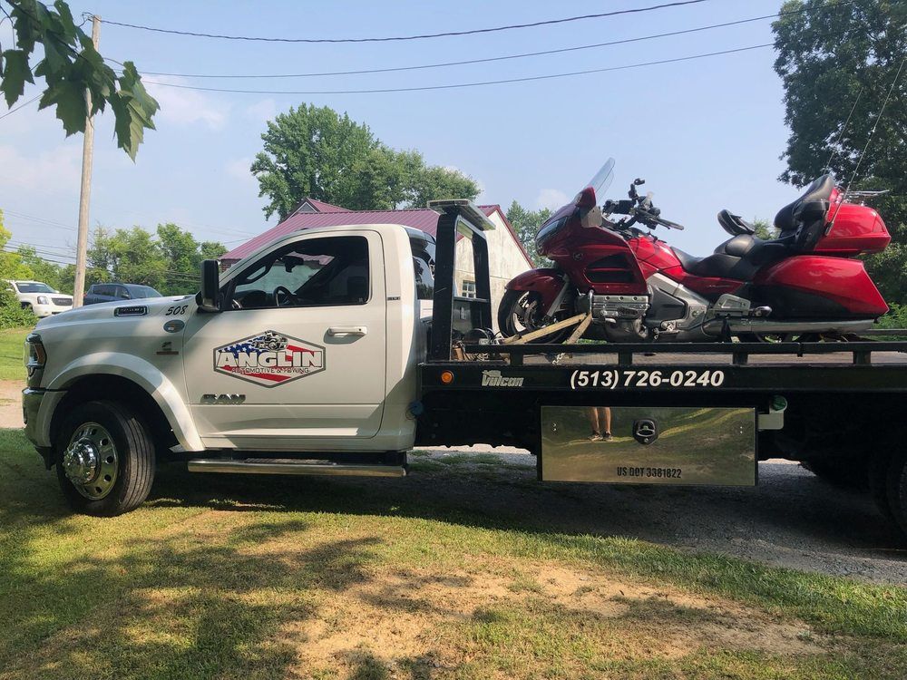 White tow truck with a red motorcycle on its bed; phone number on truck.