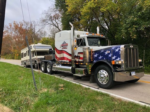 Semi-truck decorated with American flag towing a recreational vehicle on a road.