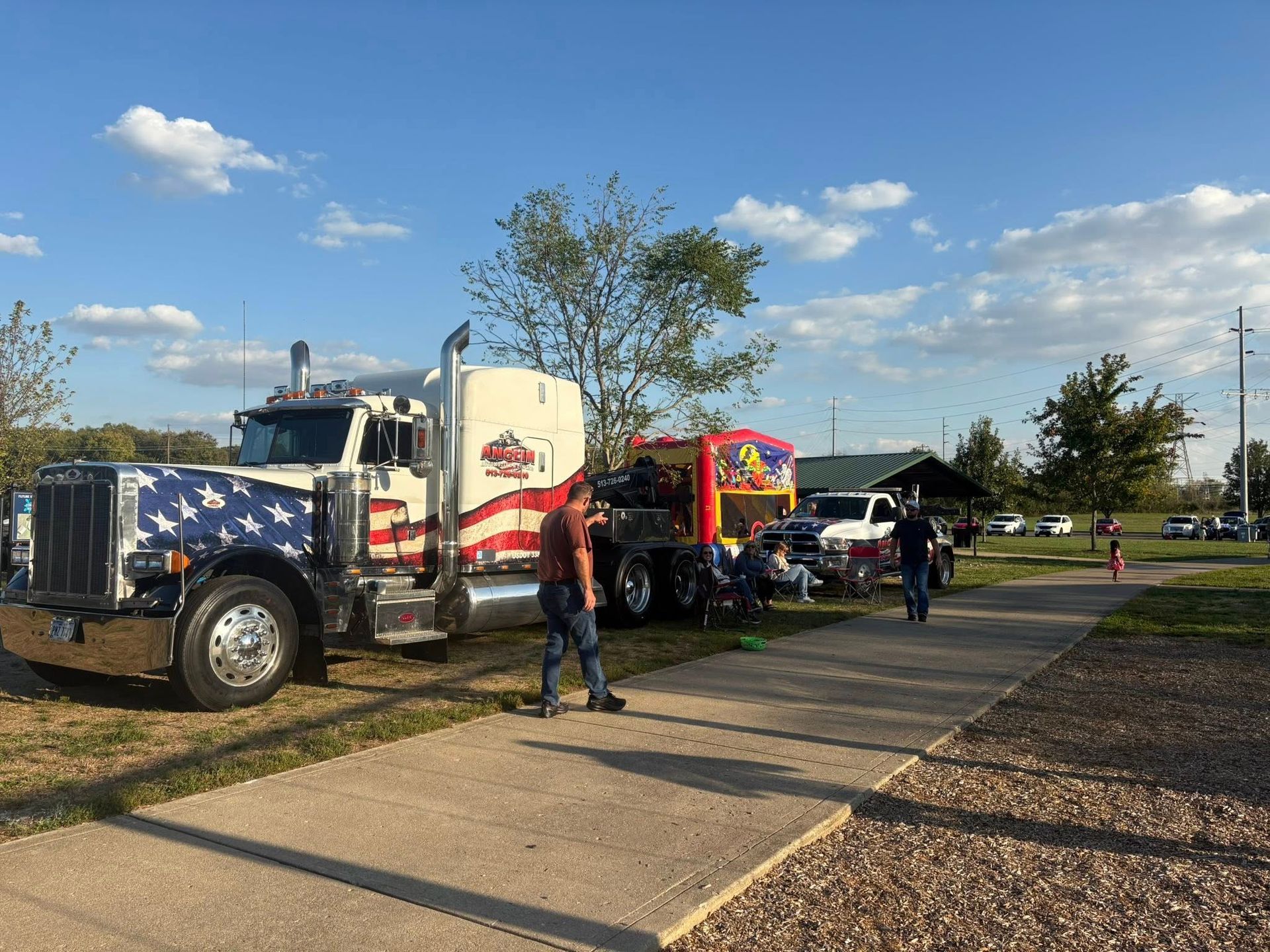 Semi-truck with American flag design parked at an outdoor event, people walking.