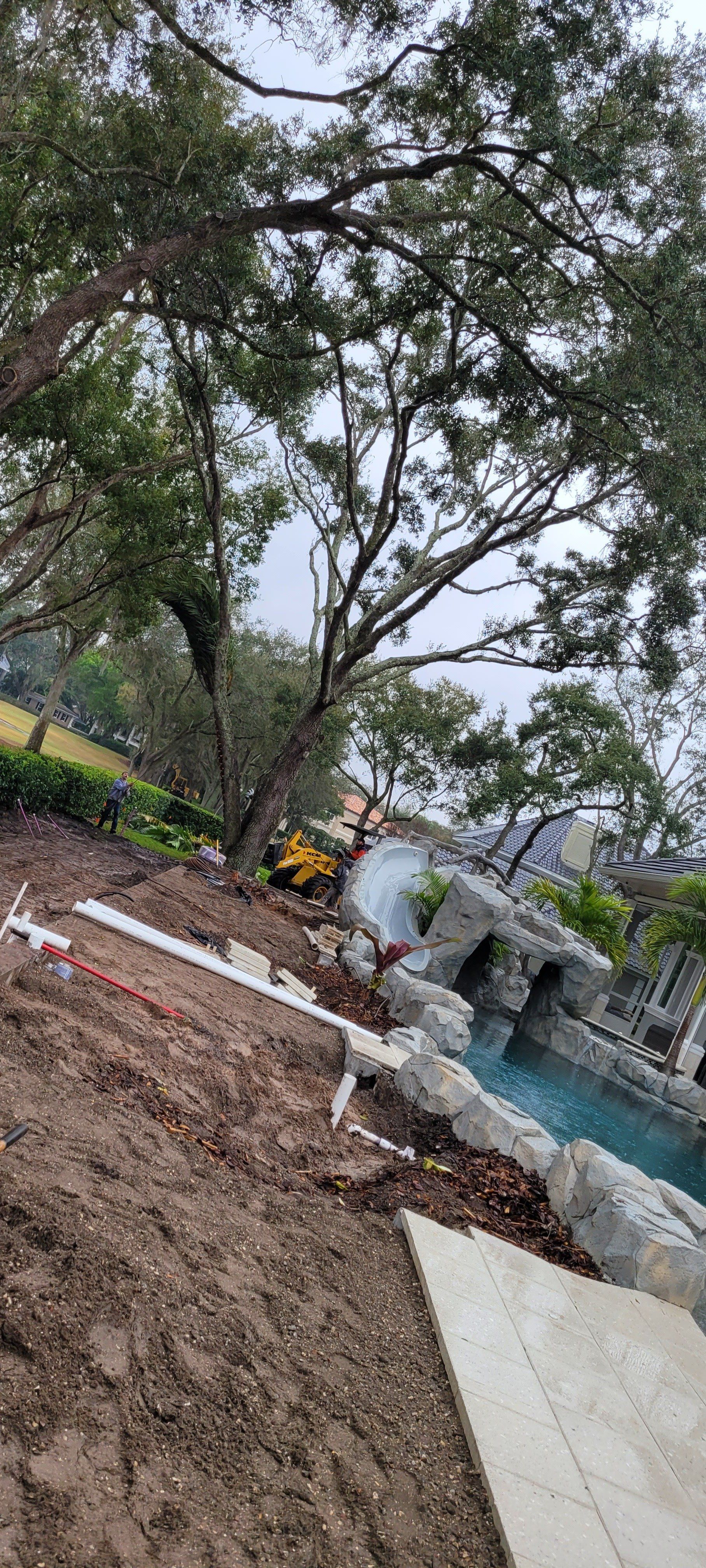 Excavation work near a pool with rock features and trees.