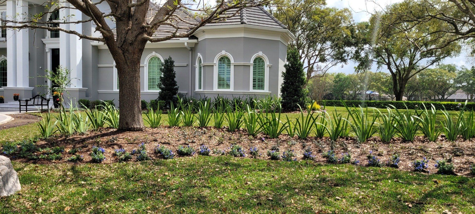 Exterior view of a gray building with a landscaped garden, trees, and green grass.