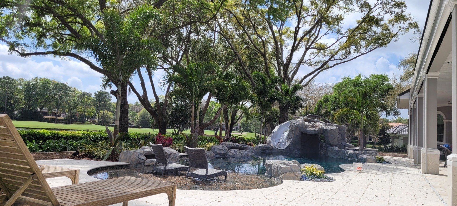 Lounge chairs on patio overlooking pool and golf course. Trees and blue sky in the background.