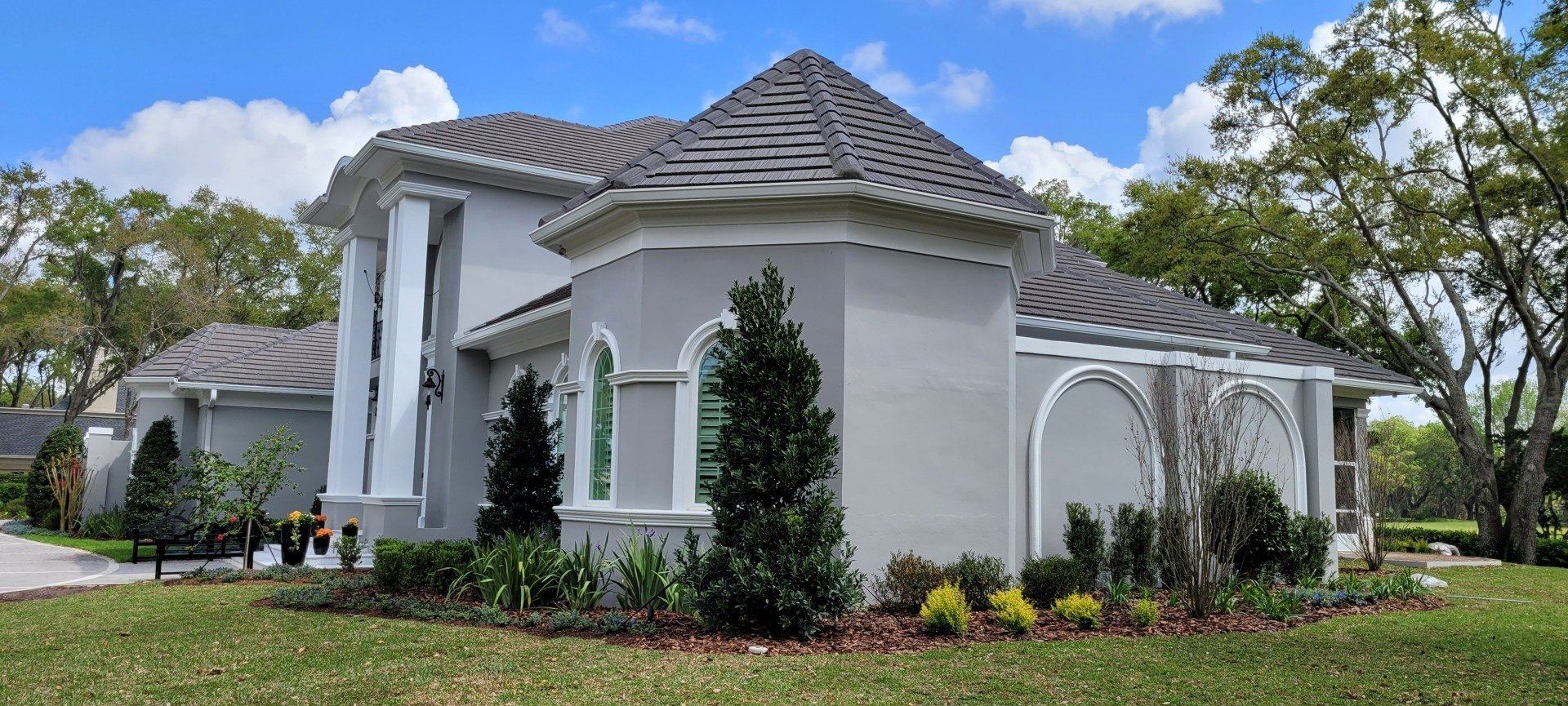 A light gray stucco house with a dark gray tile roof and well-manicured landscaping.