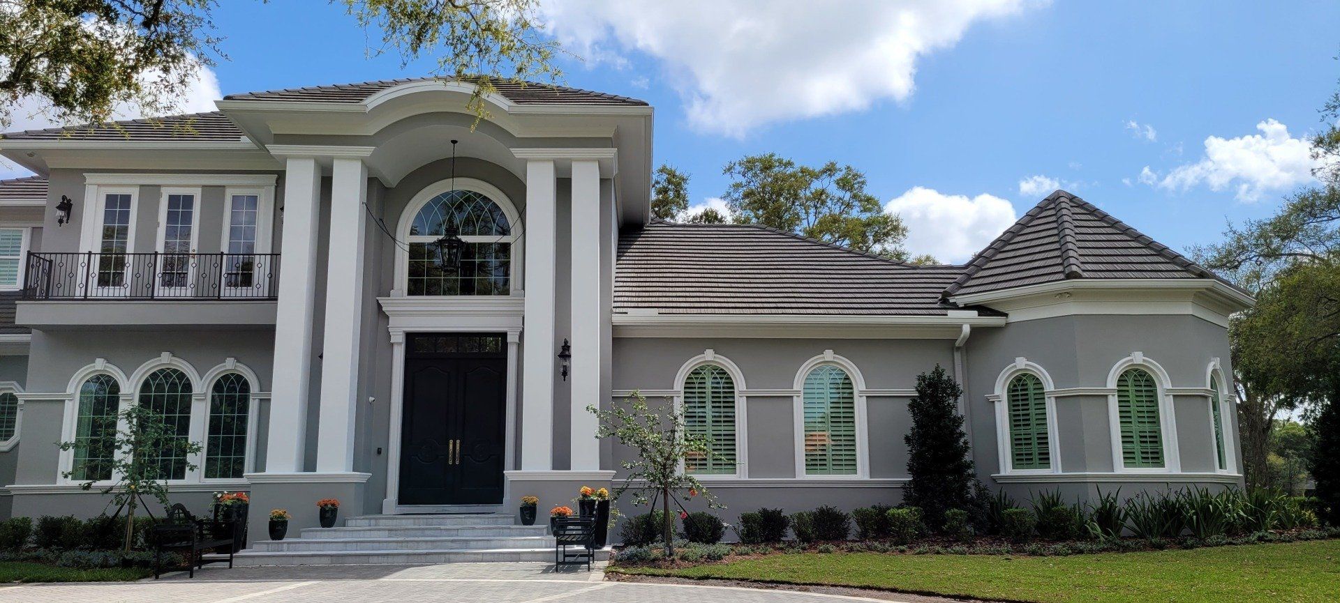Gray and white mansion with pillars and arched windows on a sunny day.