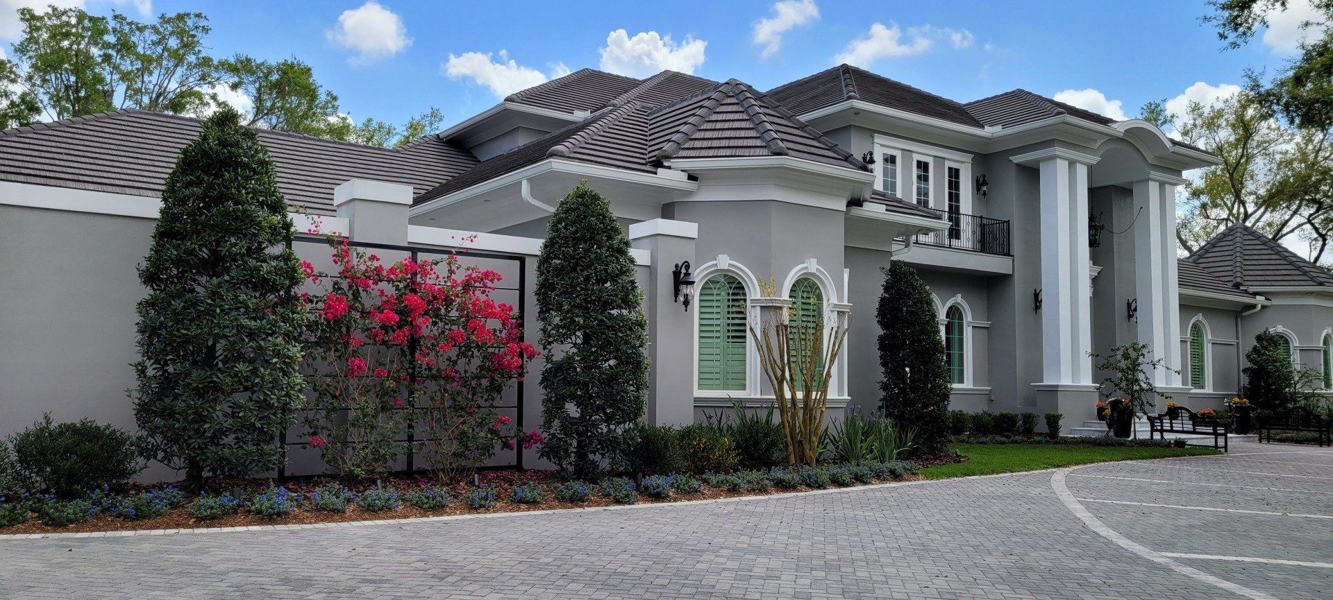 Gray mansion with pillars, a stone driveway, and landscaping.
