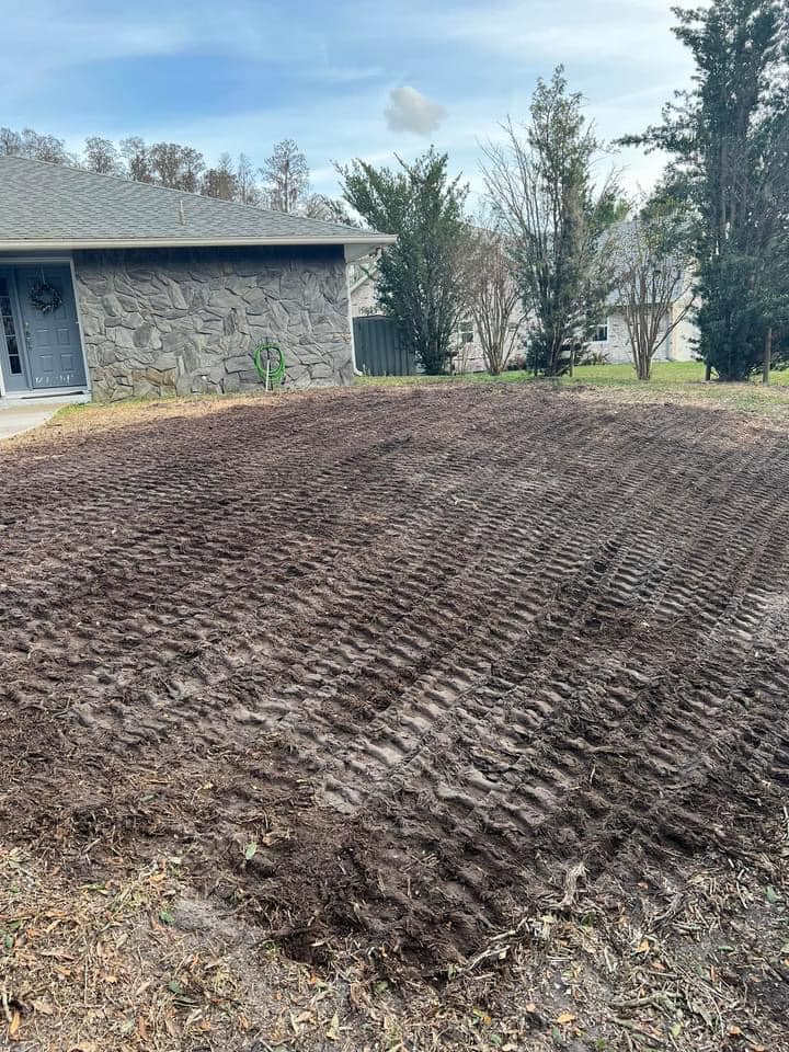 Brown soil, tractor tire tracks, house in background. Preparing for planting, outdoors.