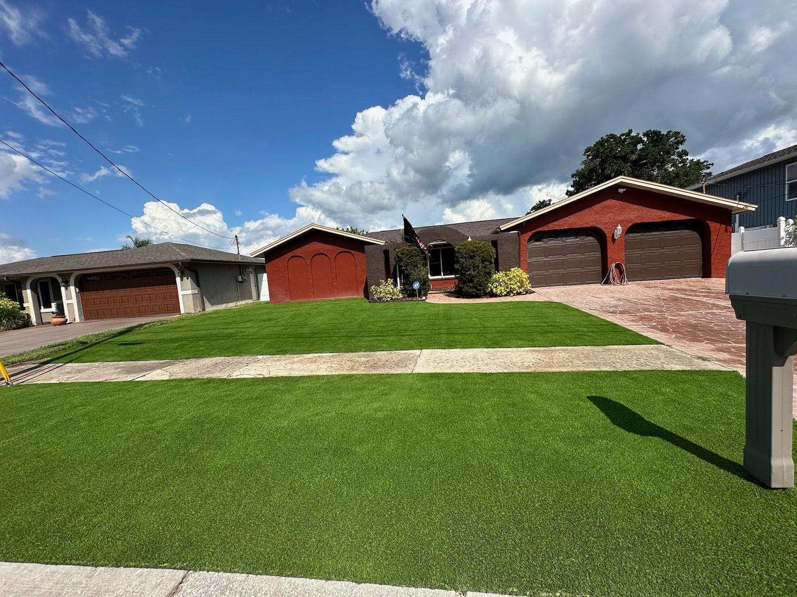 Houses with red and gray facades and brown garage doors under a cloudy blue sky, with green lawns.