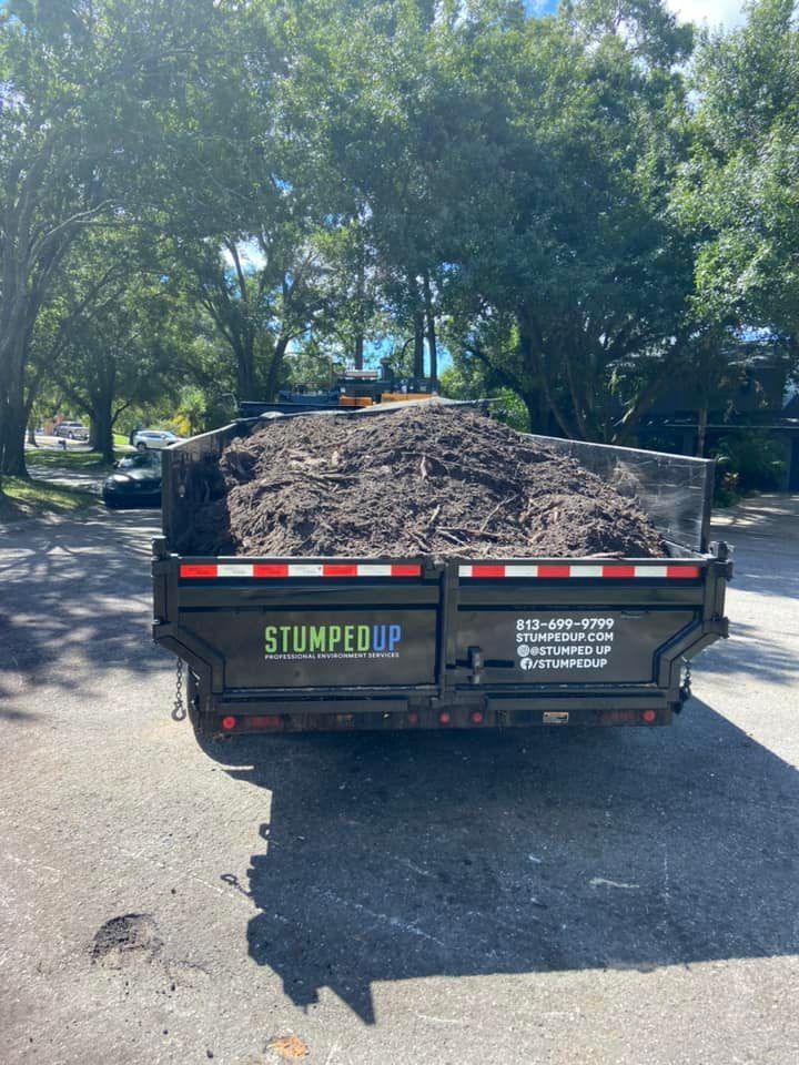 A trailer filled with dark mulch, parked on pavement, with a business name 