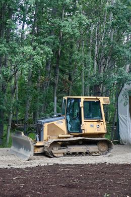Yellow bulldozer parked near trees and a building; construction site.