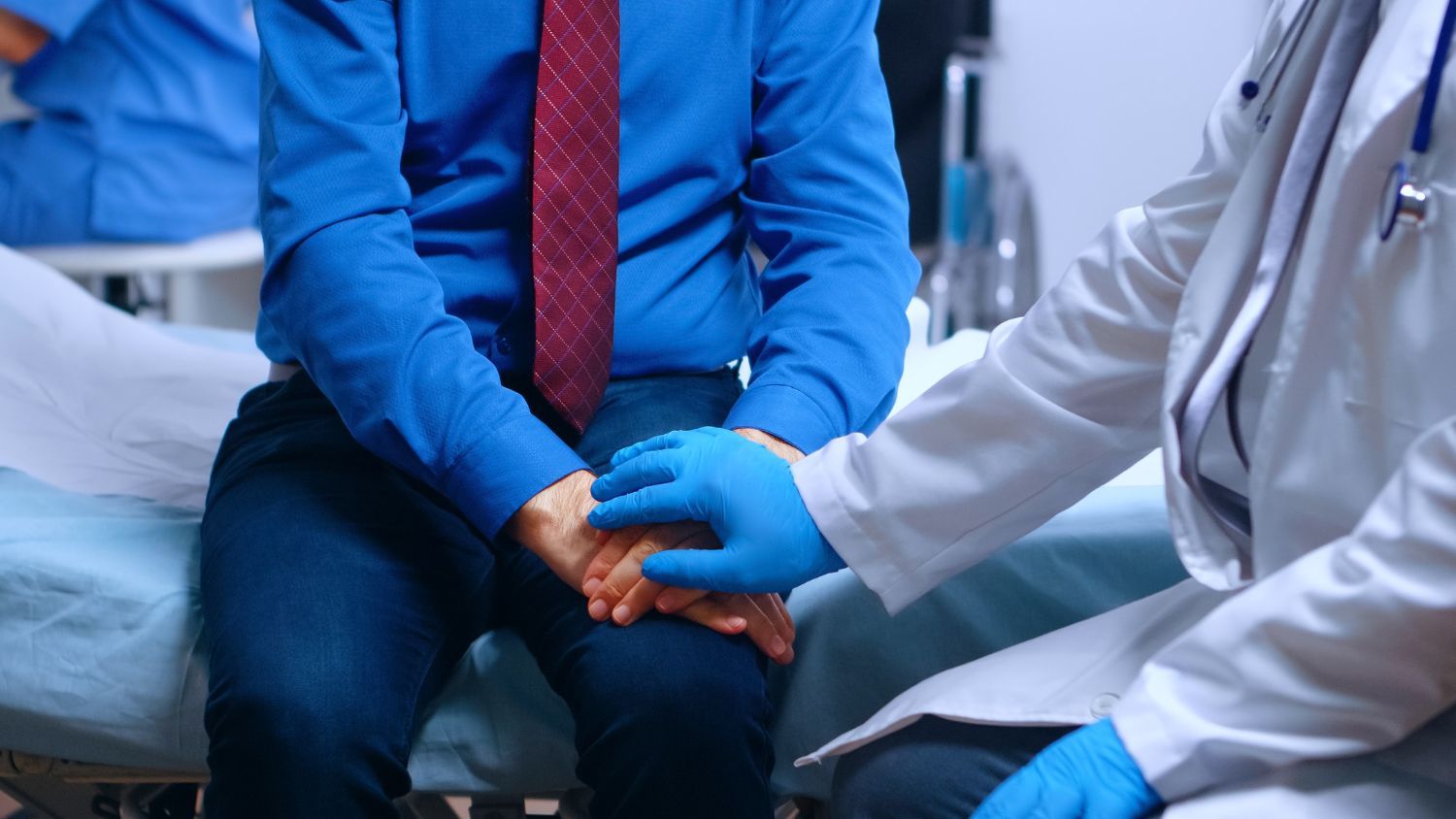A doctor is holding the hand of a patient in a hospital bed.