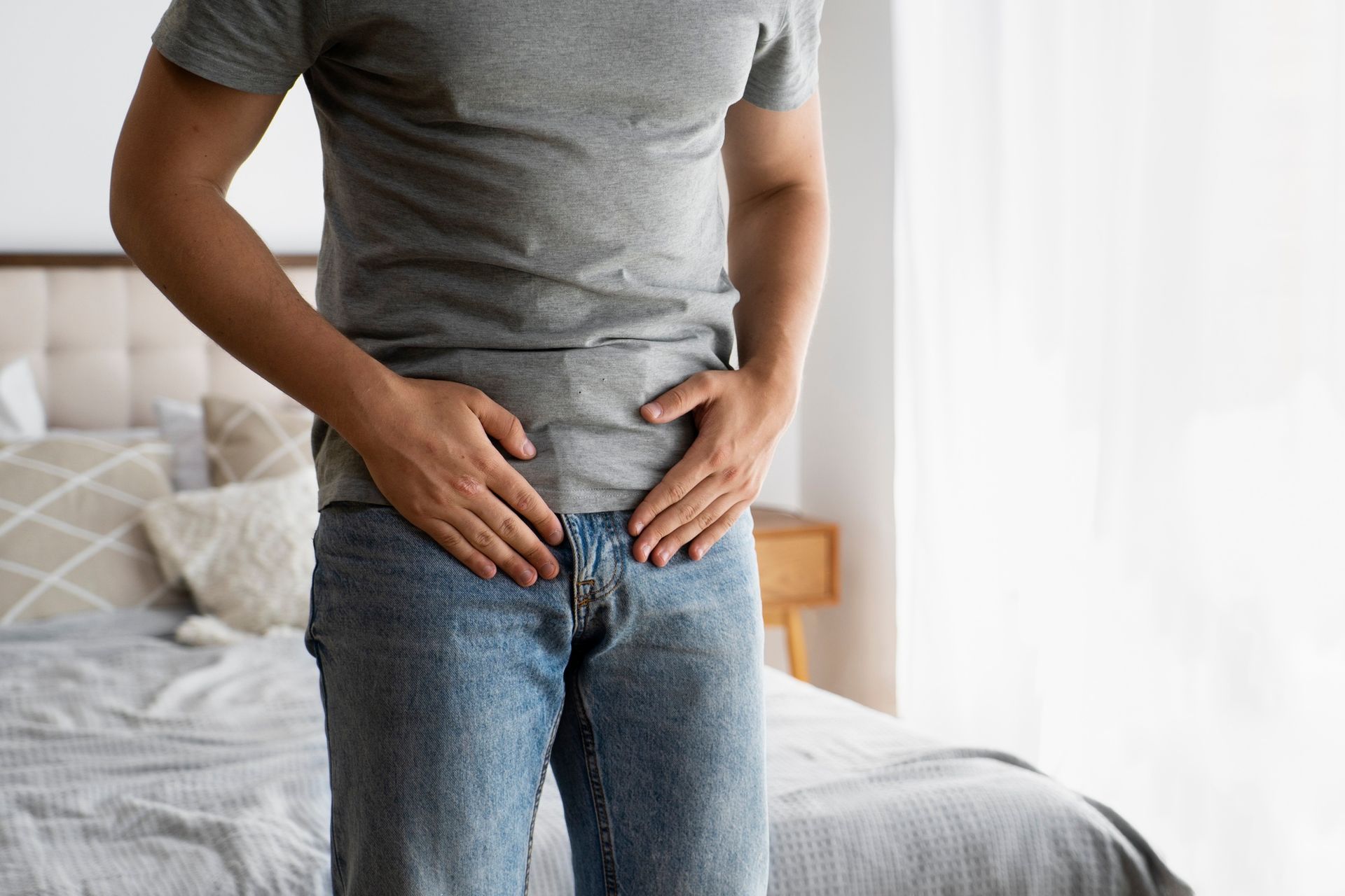 A man is standing in front of a bed with his hands on his hips.