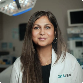Woman in a white lab coat smiles in an operating room setting.