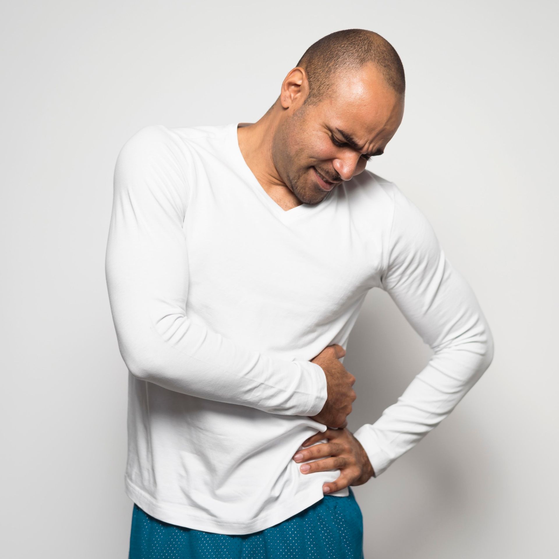 A man in a white shirt is holding his stomach in pain.