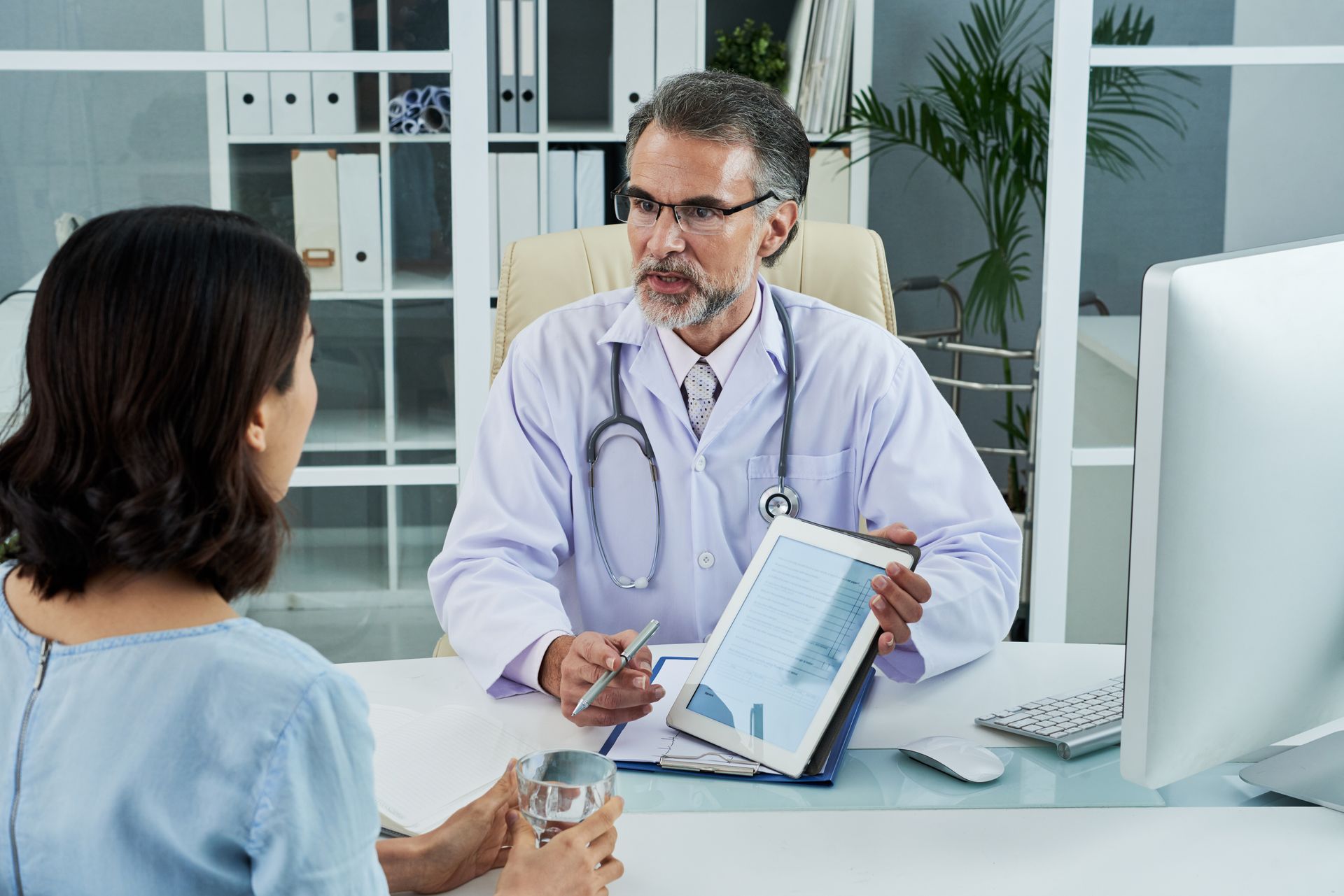 A doctor is sitting at a desk talking to a patient.