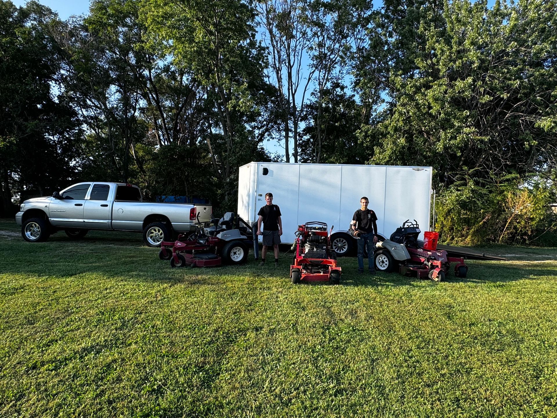 A group of people standing next to lawn mowers in a grassy field.