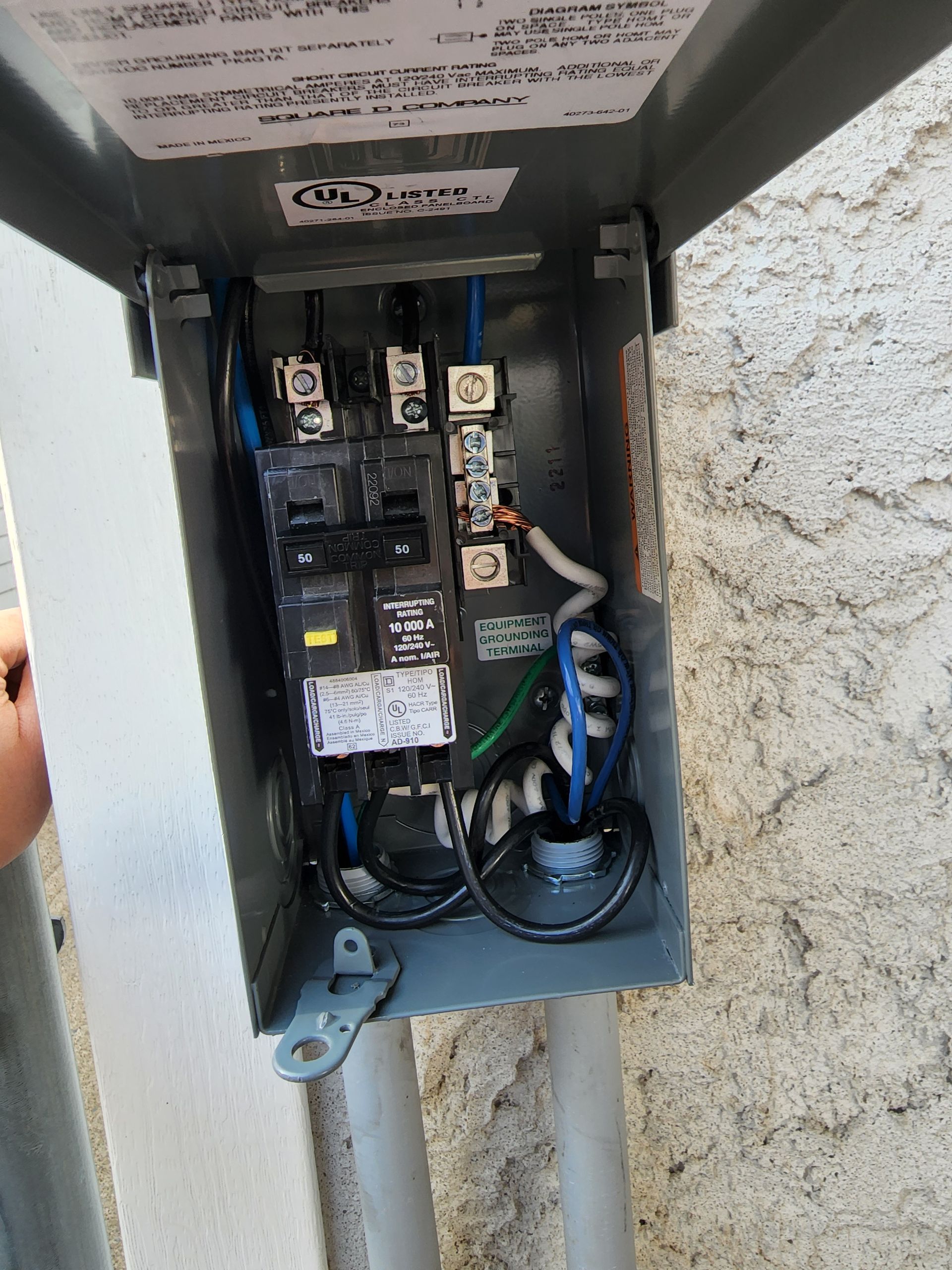 Open electrical box with circuit breakers and wiring. Blue, black, white, and green wires. Gray metal enclosure.