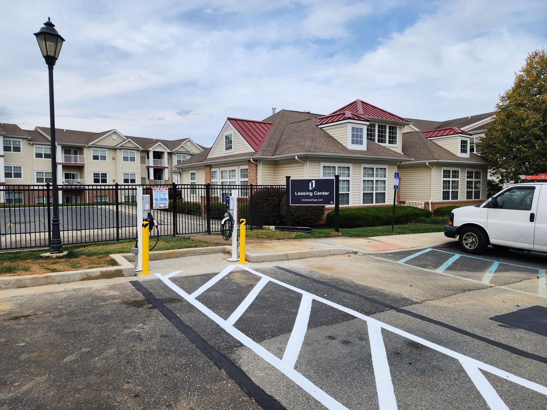 Apartment complex entrance with a gate, parking markings, and a white van parked nearby.