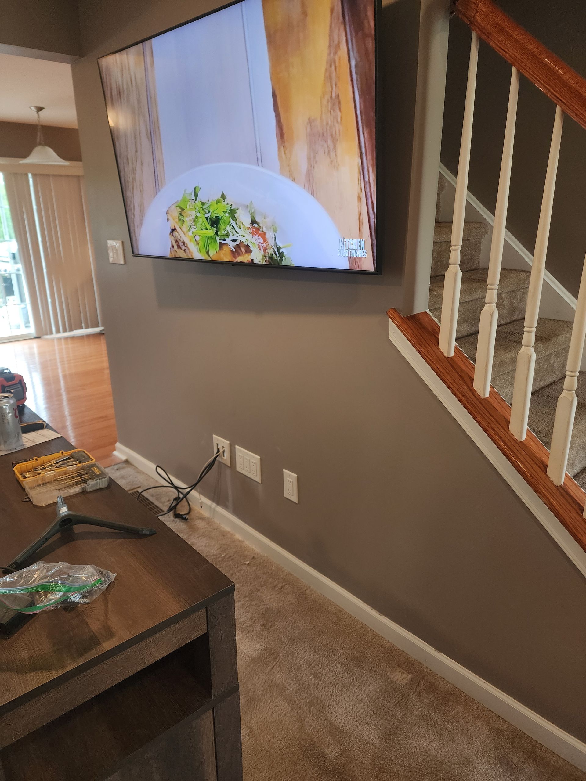 Television mounted on a brown wall, beside stairs with light-colored carpet, showing a food show.