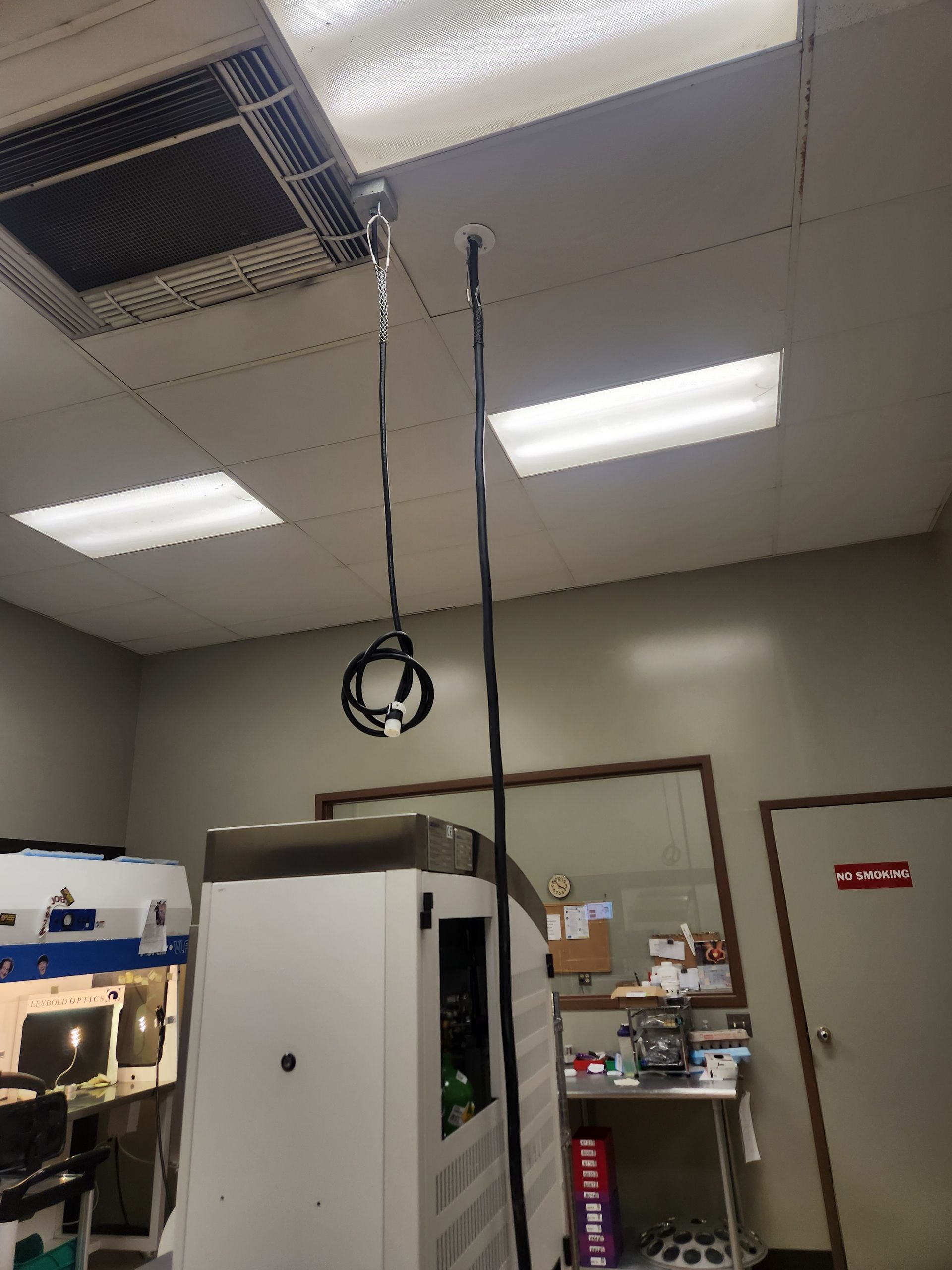 Anesthesia equipment hanging from ceiling in a clinical setting; white lights and beige walls.