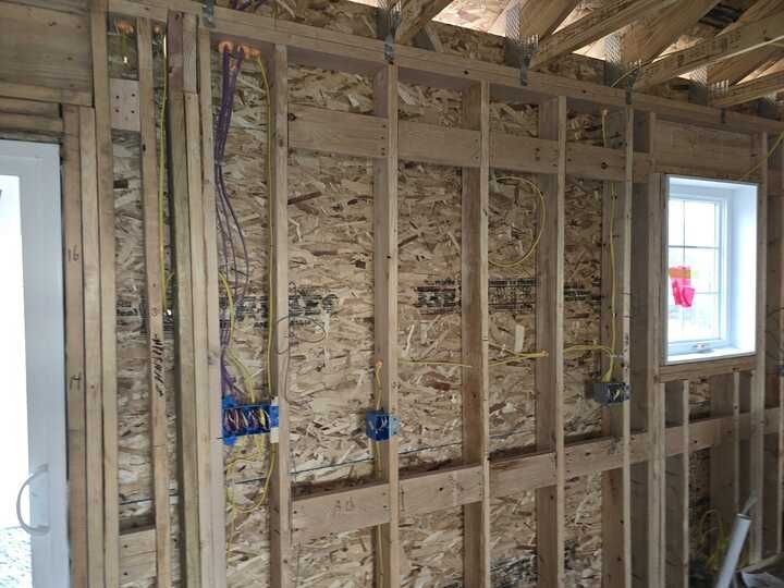 Gray wall with TV mount, wiring, electrical outlets, and tools on the floor. Staircase on right.