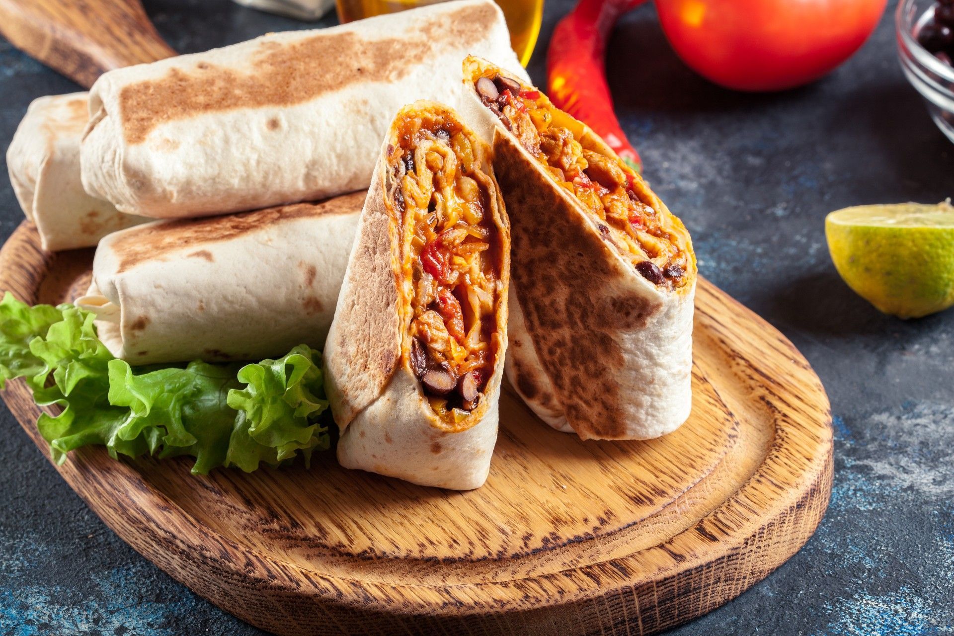 A burrito is cut in half on a wooden cutting board.