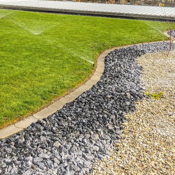 Un arroseur pulvérise de l'eau sur une pelouse verte luxuriante à côté d'un chemin de gravier.