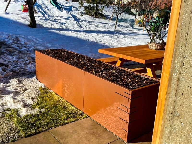 Une table de pique-nique en bois est posée dans la neige à côté d'une jardinière.