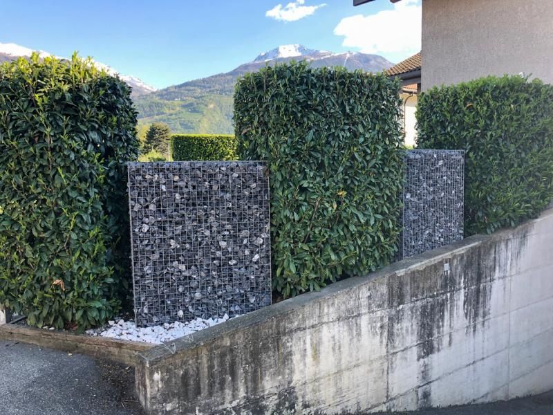 Une clôture faite de rochers et de buissons à côté d'un bâtiment avec des montagnes en arrière-plan.