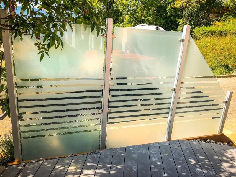 Une clôture en verre dépoli est posée sur une terrasse en bois.