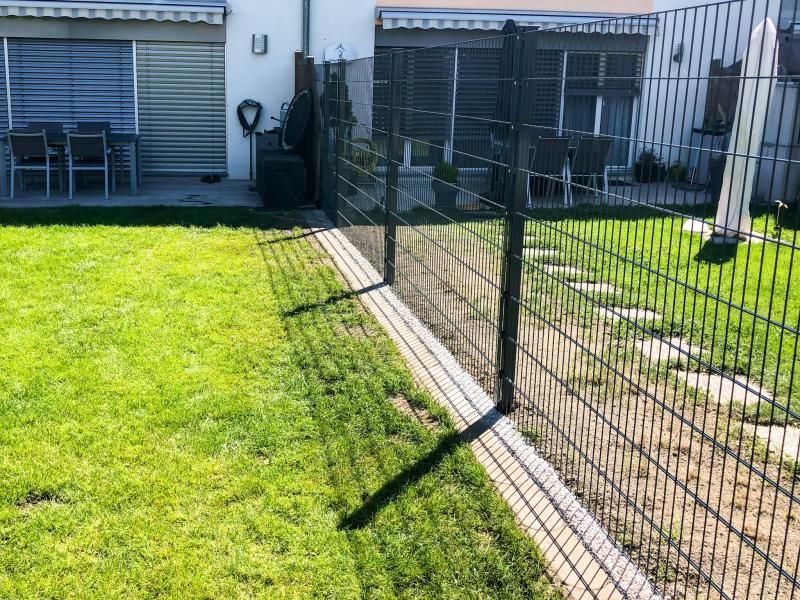 Une clôture entoure une pelouse verte luxuriante dans une cour arrière.