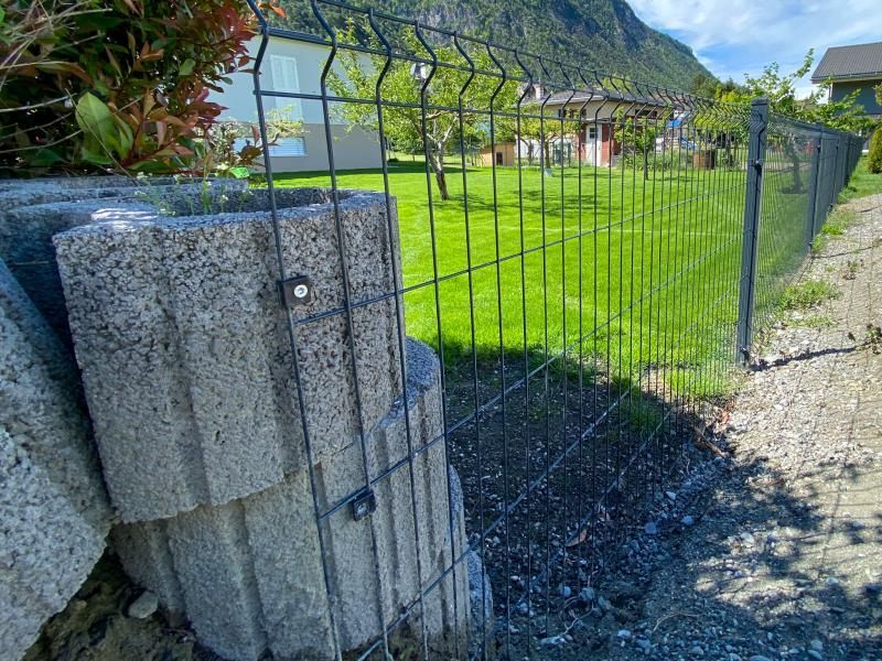 Une clôture entoure une jardinière en béton dans une cour.
