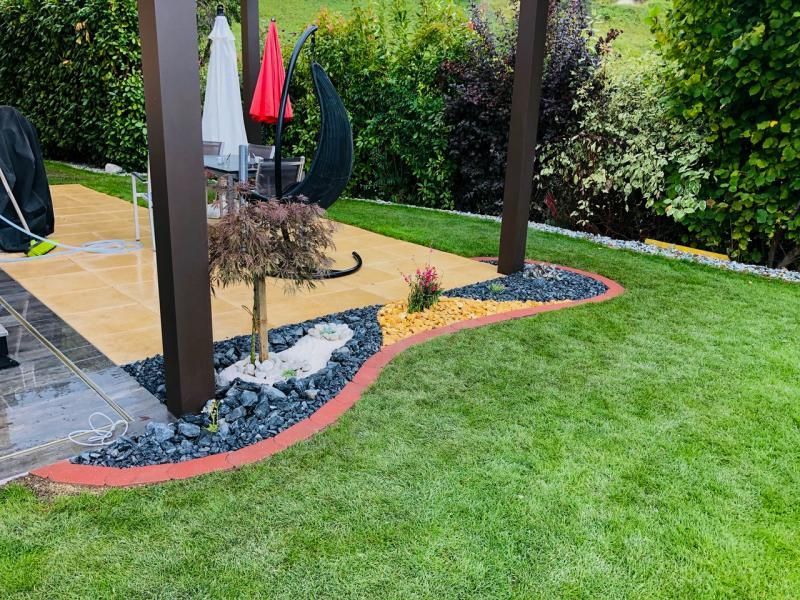 Une pelouse verte luxuriante avec une pergola et des chaises en arrière-plan.