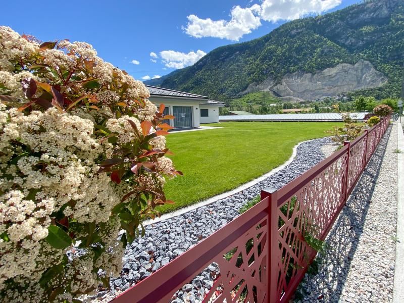 Une clôture rouge entoure un champ vert luxuriant avec des montagnes en arrière-plan