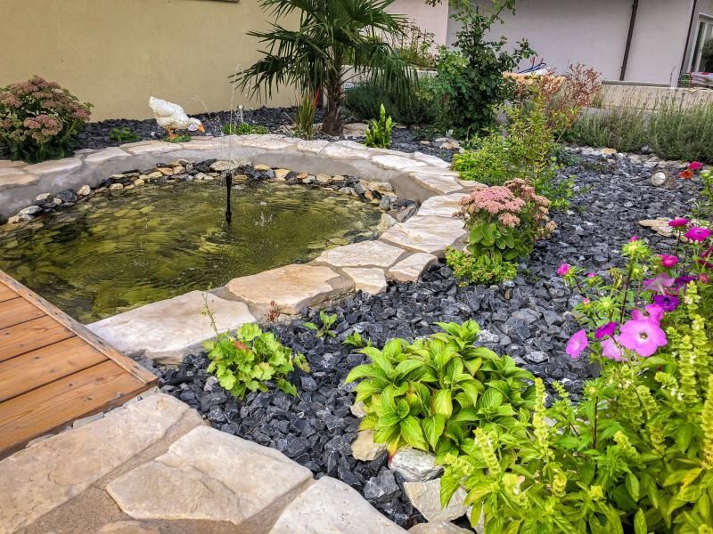 Il y a un étang au milieu du jardin entouré de rochers et de fleurs.